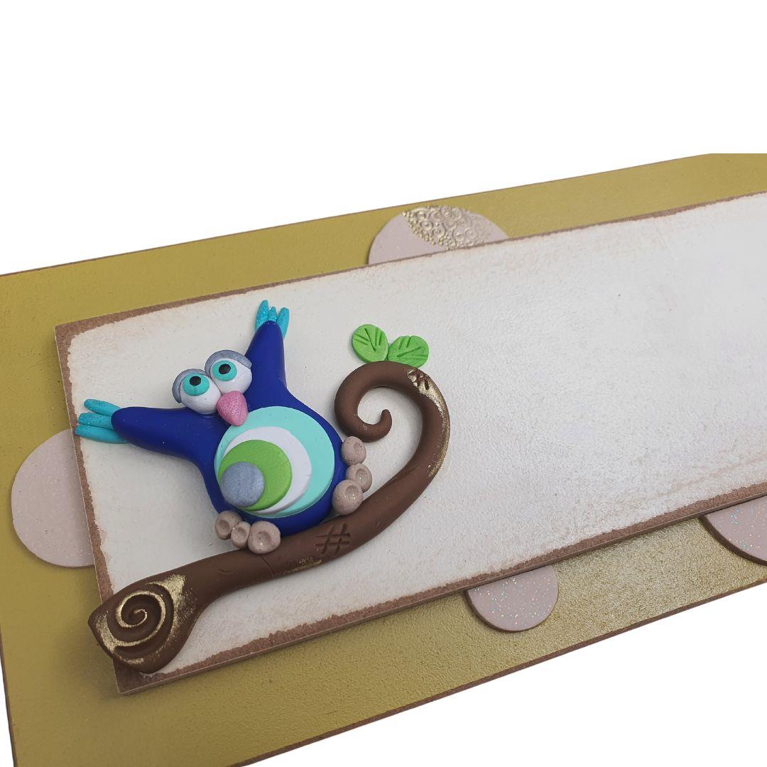 תקריב על עבודת הפיסול בחימר פולימרי של ינשוף כחול ופרחים בשלט עץ כפרי.