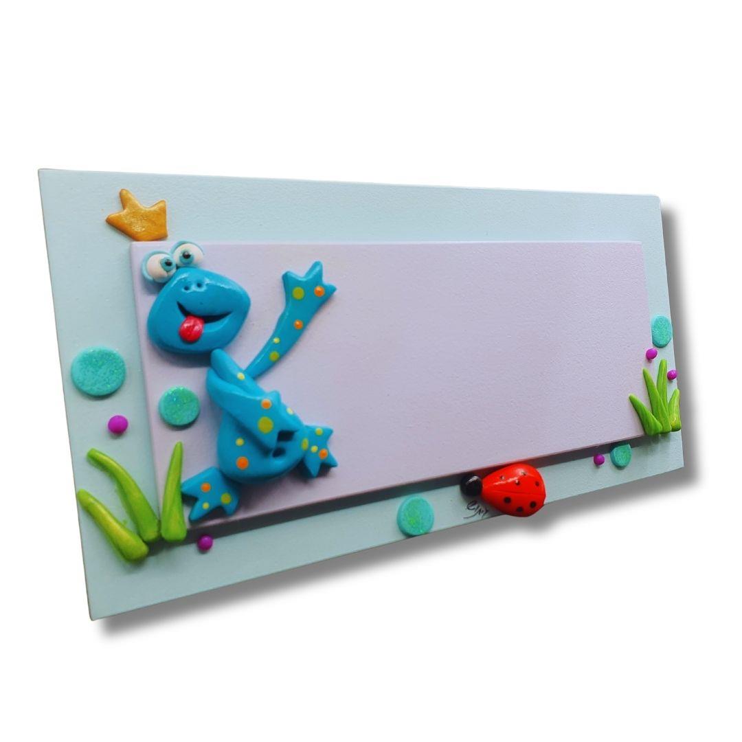 שלט צפרדע טורקיז מעץ לדלת כניסה עם דמויות חימר פולימרי עבודת יד וכתר זהוב.